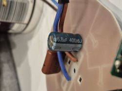 Zbliżenie na kondensator podłączony do płytki obwodu na tle innych komponentów elektronicznych.