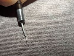 Close-up of a metal tester tip against a fabric-textured background.