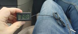 Osoba trzymająca elektroniczny termometr pokazujący 34,8°C w samochodzie.