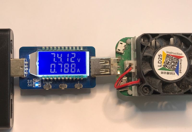 Voltage tester showing 7.412 V and 0.788 A connected to a power bank and fan-cooled load