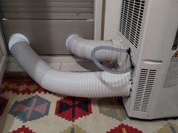 Portable air conditioner with two white corrugated hoses running to a panel in a door opening.