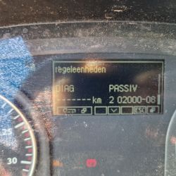 Zbliżenie na wyświetlacz samochodowy z zapalonymi kontrolkami i napisami w języku holenderskim.