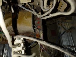 Stary transformator z widocznymi przewodami i osłonami, pokryty kurzem i lekką rdzą.