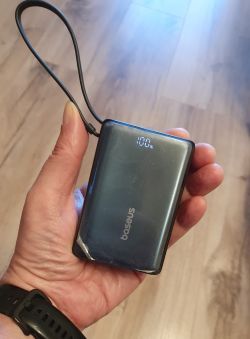 Powerbank Baseus w dłoni, na ekranie 100%, z podłączonym krótkim kabelkiem