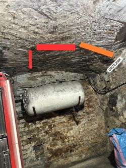 Zaczerniony sufit i wilgotna ściana w kotłowni z widocznymi instalacjami Zaczerniony sufit piwnicy z zaznaczonymi liniami i widocznym zbiornikiem ciśnieniowym