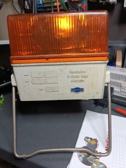 Pomarańczowa lampa ostrzegawcza DAIMON na metalowej ramce, na stole warsztatowym.