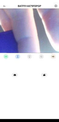 Close-up of fingers holding a blue object in front of the camera lens with an app interface in the background.