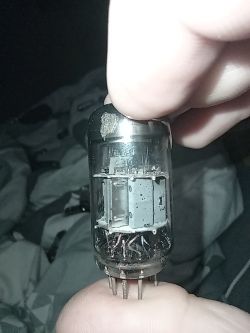 Lampa elektronowa trzymana w palcach na tle pościeli, widoczne wewnętrzne elektrody
