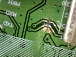 Damaged trace on green printed circuit board with visible corrosion