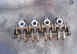 Zdjęcie mechanizmu z kilkoma okrągłymi elementami na metalowej osi, umieszczonego na betonowej powierzchni.