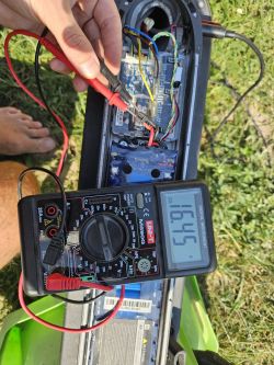 Osoba mierzy napięcie w hulajnodze elektrycznej Mi M365 za pomocą multimetru.