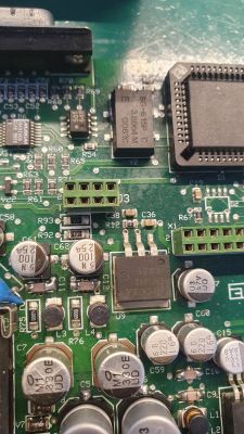 Zbliżenie na płytkę drukowaną z różnymi komponentami elektronicznymi, w tym kondensatorami, układami scalonymi i zworkami.