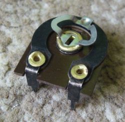 Close-up of a trimmer potentiometer with metal bracket and three pins on a fabric background