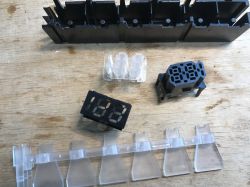 Elementy plastikowe i wyświetlacz LED z rozebranego programatora zmywarki ułożone na drewnianym blacie.