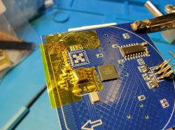 Close-up of a blue circuit board with integrated circuits and yellow insulating tape.