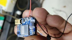Hand holding a small blue circuit board with a USB plug and thin wires