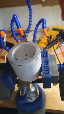 Plug secured in a vise, close-up of a hand using a screwdriver to open it.