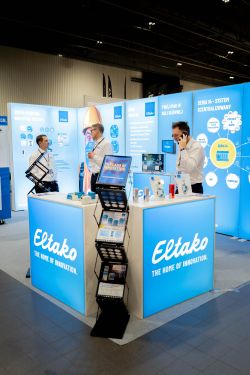 Eltako trade show booth with three men, product displays, and blue information panels.