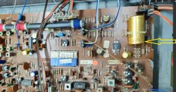 Płytka drukowana z widocznymi elementami elektronicznymi, w tym kondensator, wskazany żółtą strzałką.