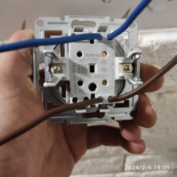 Ręka trzymająca gniazdo elektryczne z podłączonymi przewodami.