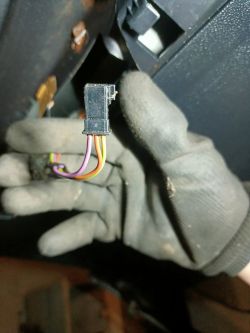 Ręka w rękawiczce trzyma złącze elektryczne z kolorowymi przewodami.