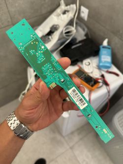 Osoba trzymająca zieloną płytkę drukowaną z komponentami elektronicznymi.