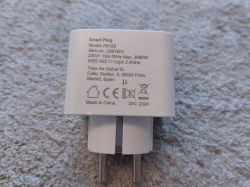 WOOX R6128 smart plug lying on a gray surface, shown from the back with technical information visible.