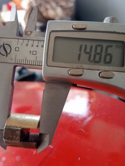 Suwmiarka cyfrowa mierząca metalowy element, wyświetlająca wartość 14.86 mm.