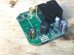 Zbliżenie na płytkę drukowaną z elementami elektronicznymi, w tym kilkoma przekaźnikami i kondensatorami.