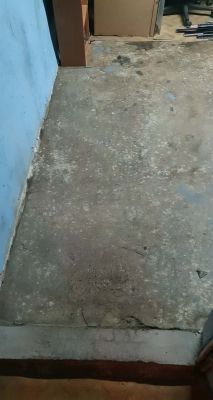 Betonowa posadzka z plamami i nierównościami przy niebieskiej ścianie w pomieszczeniu