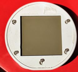 LCD display on a round base Square gray LCD display mounted on a round white base with six visible screws.