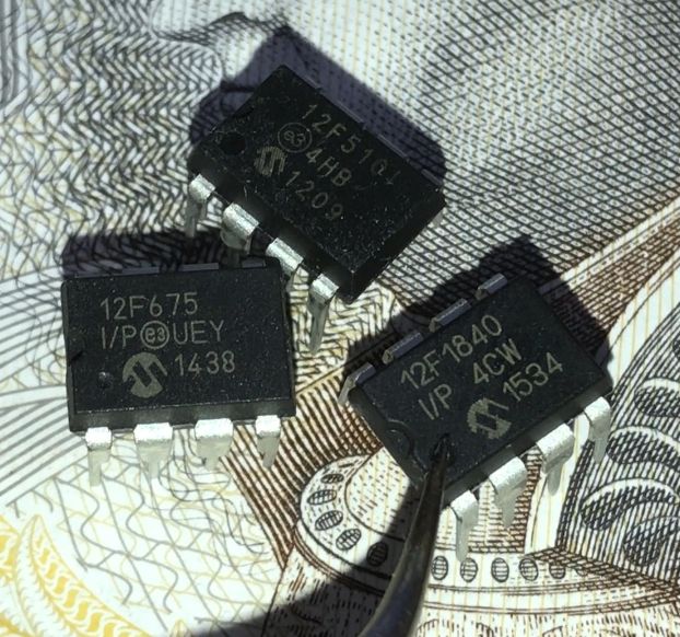 Three Microchip PIC microcontrollers on currency pattern, 12F1840 pointed by tweezers
