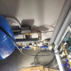 Instalacja hydrauliczna z połączeniami rur i pompą OMIS 25-60/130 w pomieszczeniu gospodarczym.