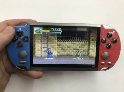 Hand holding an X12 handheld console with red and blue sides; a 2D game is shown on the screen