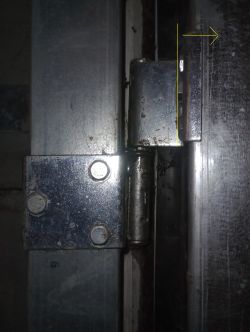 Zbliżenie na metalowy zawias bramy, pokazujący odgięcie względem ościeżnicy