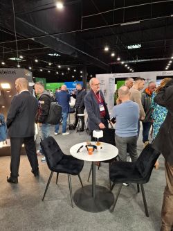 Trade show hall with people at booths; round table and two black chairs in the foreground