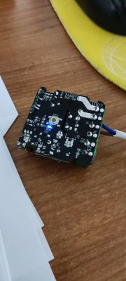 Electronic module with a lit blue LED placed on a wooden desk.