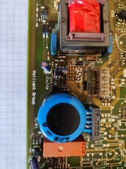 Zbliżenie płytki PCB z nadpalonymi układami scalonymi obok niebieskiego kondensatora i transformatora