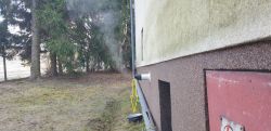 Rura wylotowa na ścianie domu z parą i garnek ustawiony pod nią na trawie