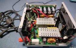 Zdjęcie urządzenia elektronicznego z otwartą obudową, pokazującego komponenty wewnętrzne takie jak kondensatory, cewki i wentylator.