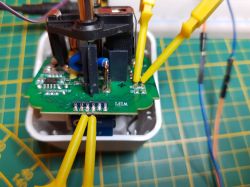 The image shows a dismantled electrical socket with an exposed circuit board and attached measurement wires.