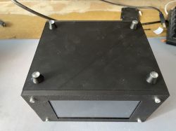 Black rectangular device with screen and four conical feet on the top surface