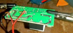 Close-up of a circuit board with soldered wires and a mounting clamp.