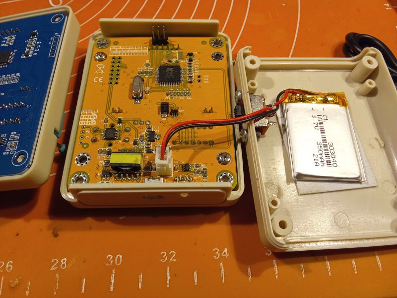 Wnętrze dwóch otwartych testerów elektronicznych, ukazujące płytki PCB i baterię.