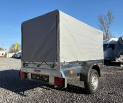 Single-axle trailer with a gray tarp cover, parked on a gravel lot outdoors
