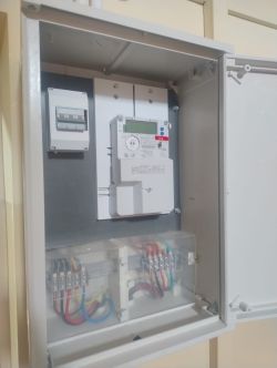 Otwarta skrzynka elektryczna z licznikiem oraz bezpiecznikami i widocznymi kolorowymi kablami.