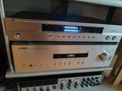 Two silver Yamaha audio components on a shelf, with lit display and front-panel knobs