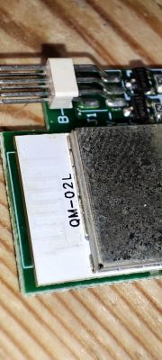 Close-up of an electronic module labeled QM-02L on a wooden surface.