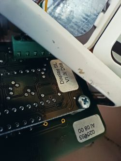 Zbliżenie na wnętrze urządzenia elektronicznego z widocznymi naklejkami i śrubą.