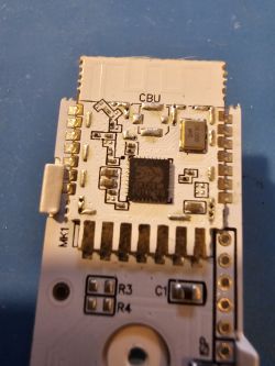 Door sensor PCB with visible pins and components Close-up of a PCB with exposed pins, a central microchip, and markings such as CBU and MK1, used in a door sensor.